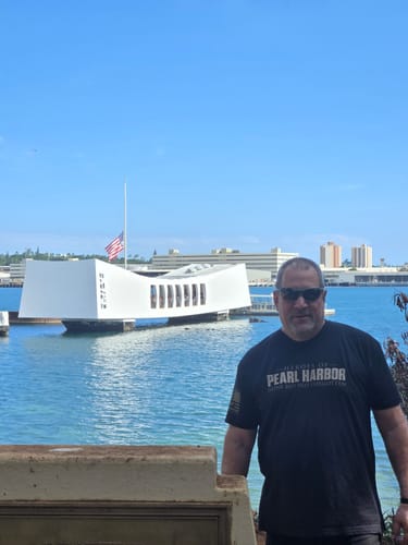 Reviewer wearing the black Heroes of Pearl Harbor shirt in front of the USS Arizona Memorial.