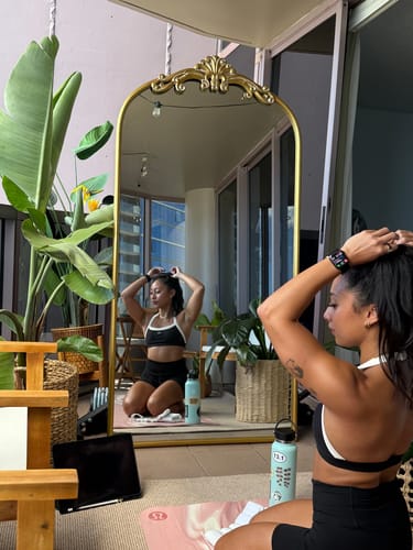 Reviewer kneeling in front of a mirror, showing the front and side of The Halter Bra in black and cream.