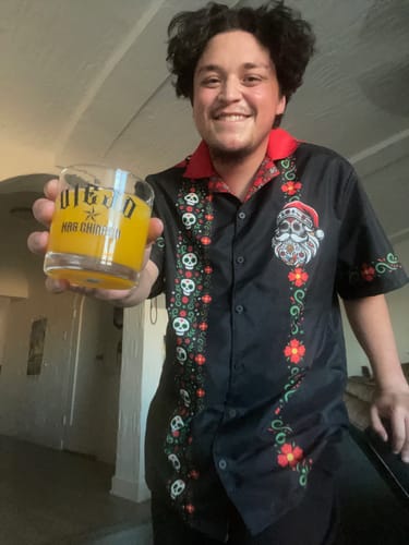 Customer smiling while wearing the black El Sancho Clause Guayabera shirt with its Santa sugar skull print.