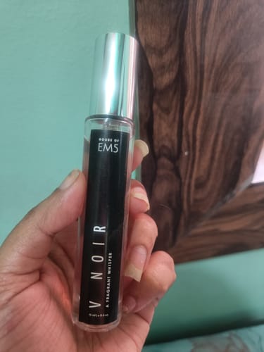 A customer's hand holding the V Noir Eau De Parfum bottle, showing its black label and silver cap.