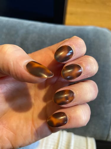 Close-up of a reviewer's hand wearing the short, oval Molten Mocha press-on nails with a glossy finish.