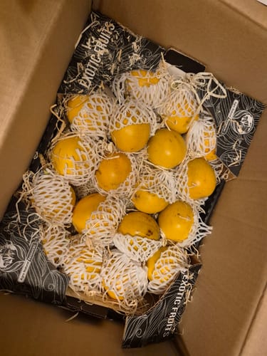 Kundenfoto der Süßen Granadillas in der offenen Versandbox. Jede Frucht ist in einem weißen Schutznetz verpackt.