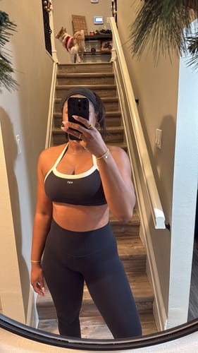 Customer takes a mirror selfie wearing The Halter Bra in black-cream with matching leggings.