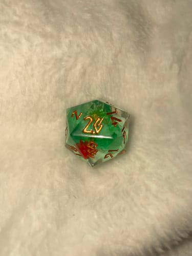 Customer's close-up of a single green Lotus Blossom d20 die with a red flower inclusion and gold numbers, resting on a white blanket.