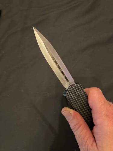 Reviewer holding the Carbon Fiber Ghost OTF Knife with its extended dagger-style blade.