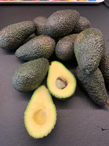 Ein Kunde zeigt eine aufgeschnittene, cremige Maluma-Avocado neben mehreren ganzen Früchten.