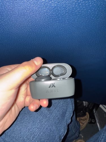 Customer holding the grey XCOR PRO earbuds in their open charging case while seated.