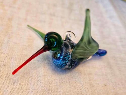 Customer's Dichroic Twist Glass Hummingbird from the side, highlighting its long red beak and dark green head.