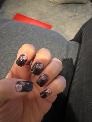 Hand einer Kundin, die ihre Maniküre mit den Midnight Foliage UV-Gel-Nagelfolien nach zwei Wochen Tragezeit zeigt.