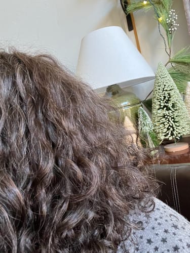 Reviewer shows their dark brown, curly hair after using the Instant Dye Shampoo.