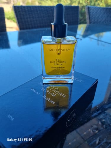 Reviewer's golden Sea Buckthorn Serum in a clear bottle, resting on its packaging box outdoors.