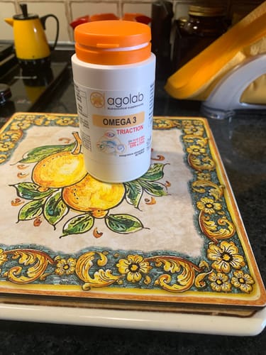 Recensore mostra il flacone di Agolab Omega 3 Triaction appoggiato su un sottopentola decorato in cucina.