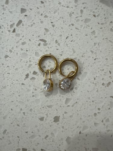 Customer's pair of gold Diamond Lock Earrings with oval zirconia charms on a counter.