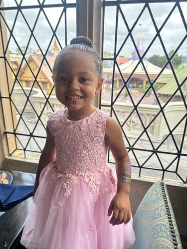Reviewer's child smiles in a pink dress, with the Dinosaur temporary safety tattoo visible on her arm.