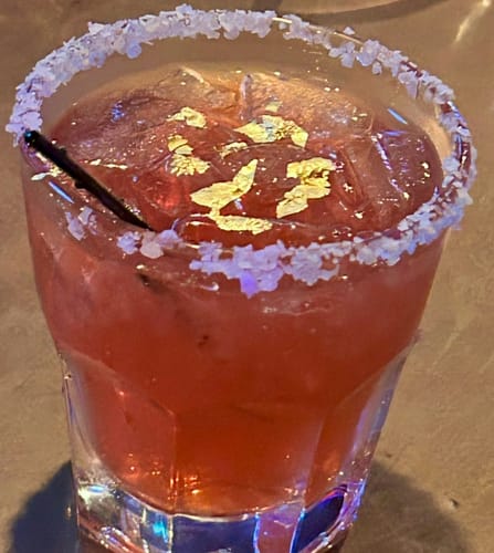 Customer's finished pink cocktail made with a mixer, served in a glass with a salted rim and gold flakes.