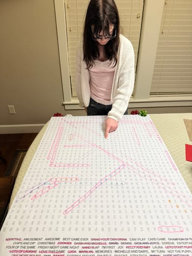 Customer leaning over the Santa's Workshop Giant Word Search Puzzle on a table, with several words already circled.