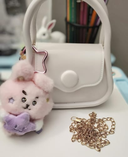 Customer's small white satchel with a keychain, sitting on a desk next to its detached gold chain strap.