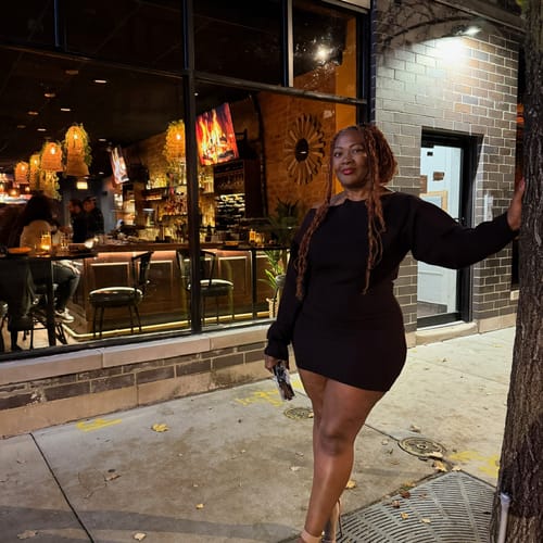 Reviewer wearing the black Knit Off-Shoulder Mini Dress outdoors at night. The dress is fitted and styled off one shoulder.