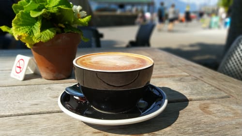Reviewer's Mr Smooth coffee, served with creamy latte art in a black cup on an outdoor table.