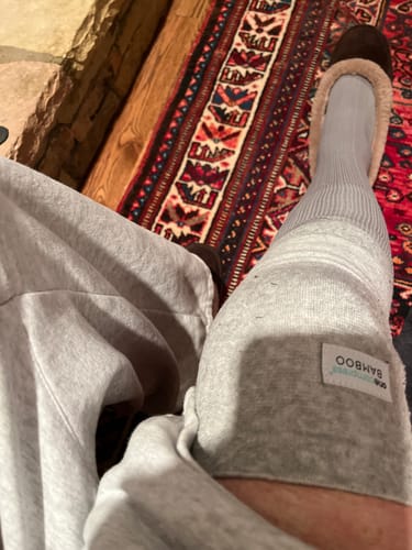 A customer wearing the light grey Premium Bamboo Knee Sleeve on their leg while relaxing on a rug.