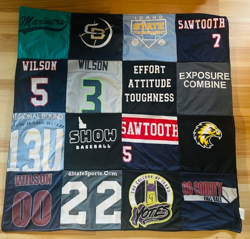 Customer's finished Premium T Shirt Quilt made from a patchwork of colorful sports jerseys, laid out on a floor.