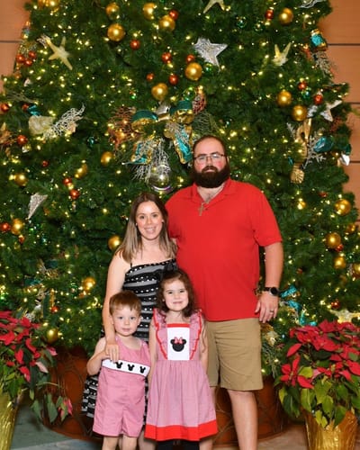 A customer's daughter wears the Magical Mouse Ears Waterfall Dress while posing with her family in front of a Christmas tree.