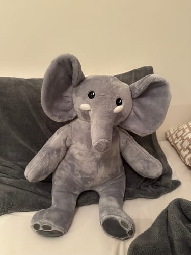Recensent toont de zachte, grijze verzwaringsknuffel olifant zittend op een bed.