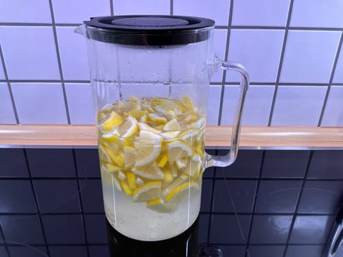 Ein Kunde zeigt die Zubereitung von Limonade mit geschnittenen Amalfi Bio-Zitronen in einem Glaskrug.