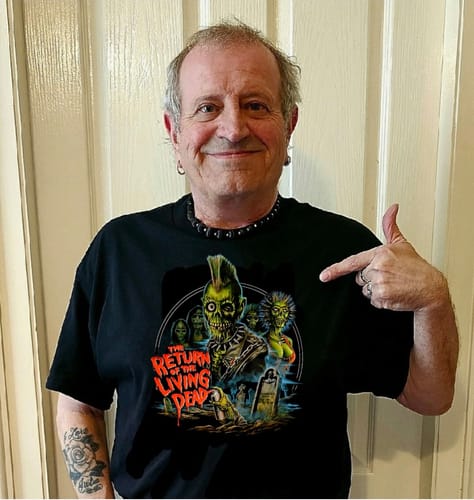 Reviewer smiling while wearing and pointing to a black unisex t-shirt with 'The Return of the Living Dead' graphic.