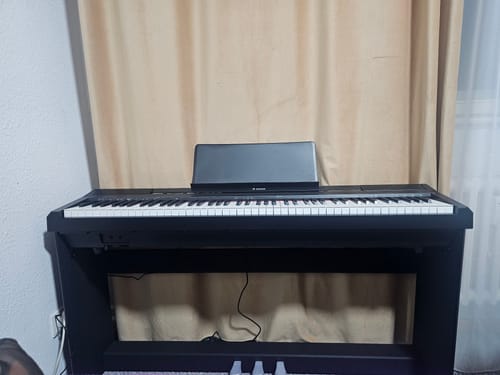 Rezensent zeigt das schwarze Donner DEP-10 Digitalpiano, das in einem Raum aufgestellt ist.