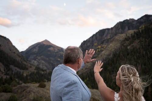 Customer and his wife holding up their hands, displaying his warrantied replacement ring in a mountain setting.