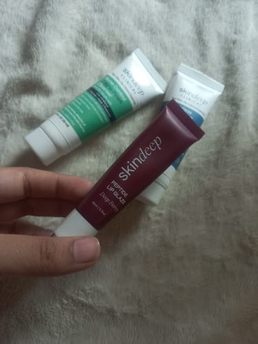 Customer holding a tube of Peptide Lip Glaze in the shade Deep Berry, with other skincare products in the background.