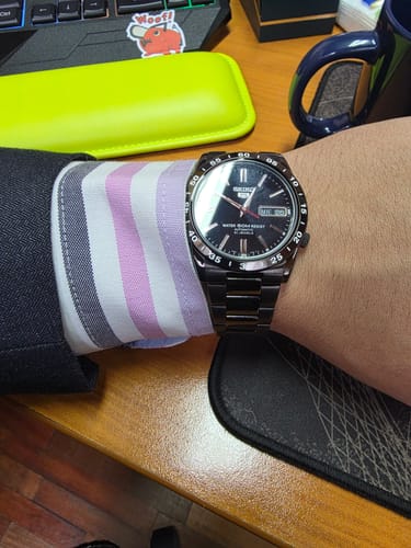 Un cliente lleva puesto el reloj Seiko 5 con correa metálica y esfera negra en la muñeca, con una camisa de vestir.