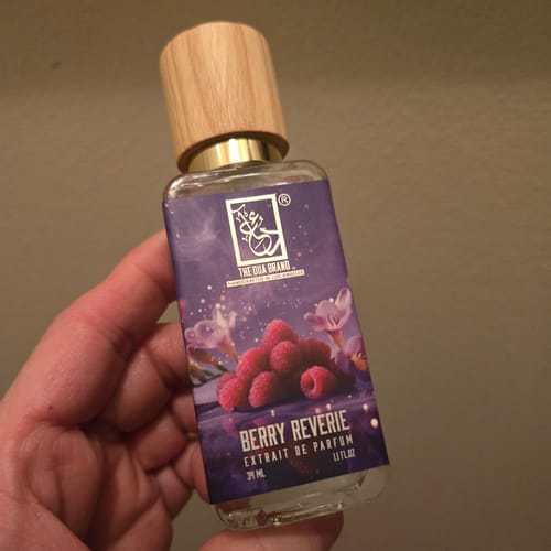 Customer holding a bottle of Berry Reverie perfume, showing the purple raspberry-themed label and wooden cap.