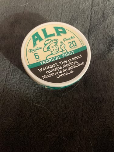 Customer's close-up of the tin of ALP Tropical Fruit Nicotine Pouches on a dark textured surface.
