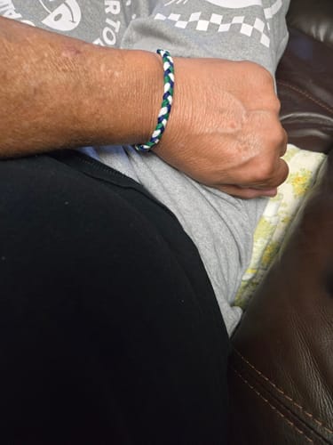 A reviewer's arm wearing the woven DAVID Bracelet in blue, white, and green while resting.