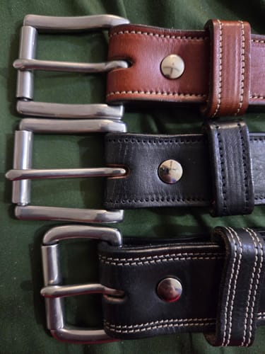 Close-up of a reviewer's three thick leather belts, including the Premier Double Layer, showing the silver roller buckles.