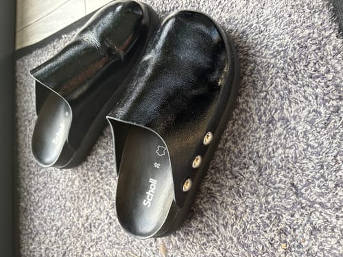 Reviewer's pair of shiny black slip-on clogs resting on a carpet.