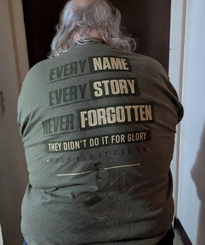 Reviewer from behind wearing a green T.V.P. Elite Membership shirt with 'NEVER FORGOTTEN' text on the back.