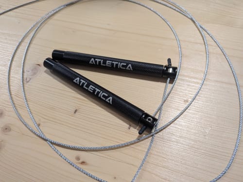 Rezensent zeigt das J2 Speed Rope mit schwarzen Griffen und Stahlseil, ausgebreitet auf einer Holzoberfläche.