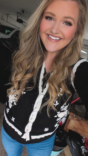 Customer smiling while wearing the black antique floral embroidered sweater vest over a black top and jeans.