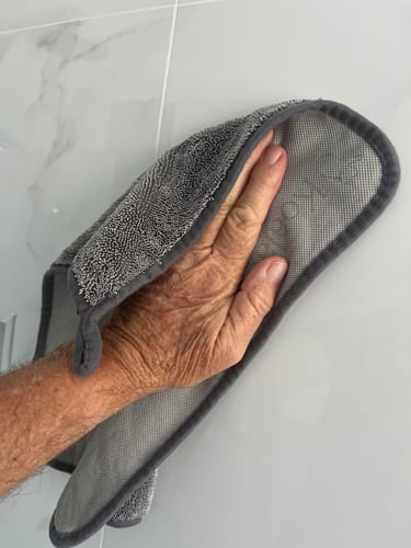 Close-up of a customer's hand using the grey KoalaCloth Mini to wipe a glossy white tile.