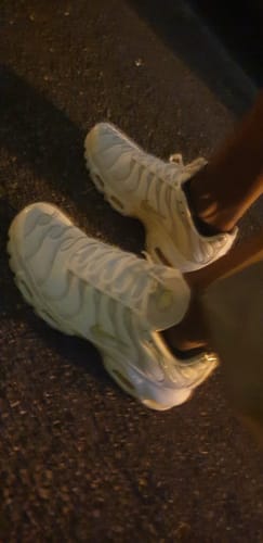 Partial view of a reviewer wearing the white Nike Air Max Plus TN sneakers at night.