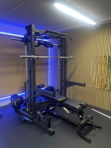 Ein Kunde zeigt sein R7 Nemesis, das in einem Heim-Fitnessstudio mit einer verstellbaren Hantelbank aufgebaut ist.