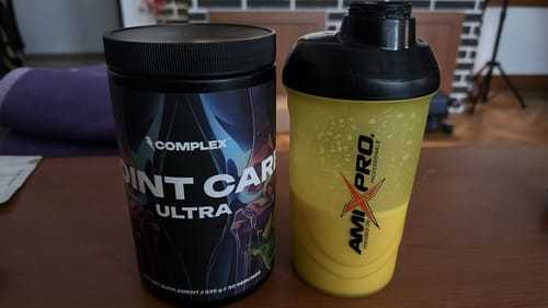 Customer's tub of Complex Joint Care Ultra next to a shaker bottle containing the prepared yellow drink.