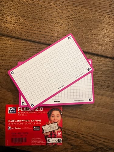 Un client montre les flashcards FLASH 2.0 quadrillées avec une bordure rose, posées sur leur emballage d'origine.