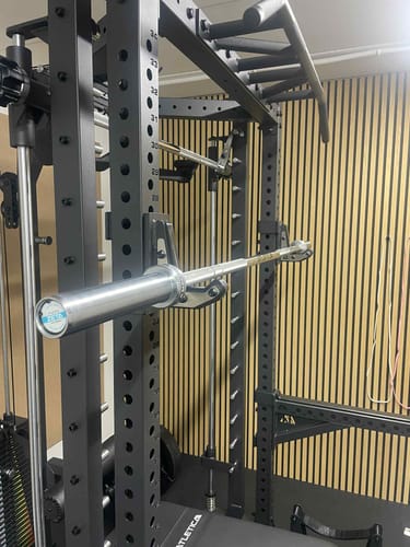 Die kompakte Zeta Langhantel eines Kunden, die auf einem schwarzen Power Rack in einem Home-Gym ruht.