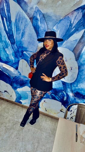 Customer wearing the Naked Print Mock Neck Top and matching leggings, styled with a black vest and a wide-brimmed hat.