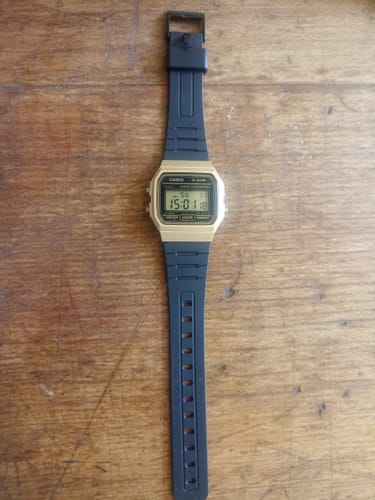 El cliente muestra su reloj Casio Vintage F-91WM-9ADF dorado y negro extendido sobre una superficie de madera.