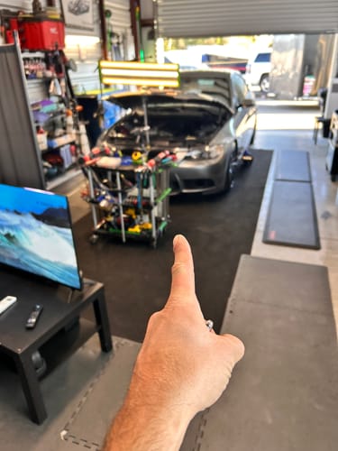 Reviewer in a workshop pointing to a cart of new paintless dent repair tools next to a car being serviced.